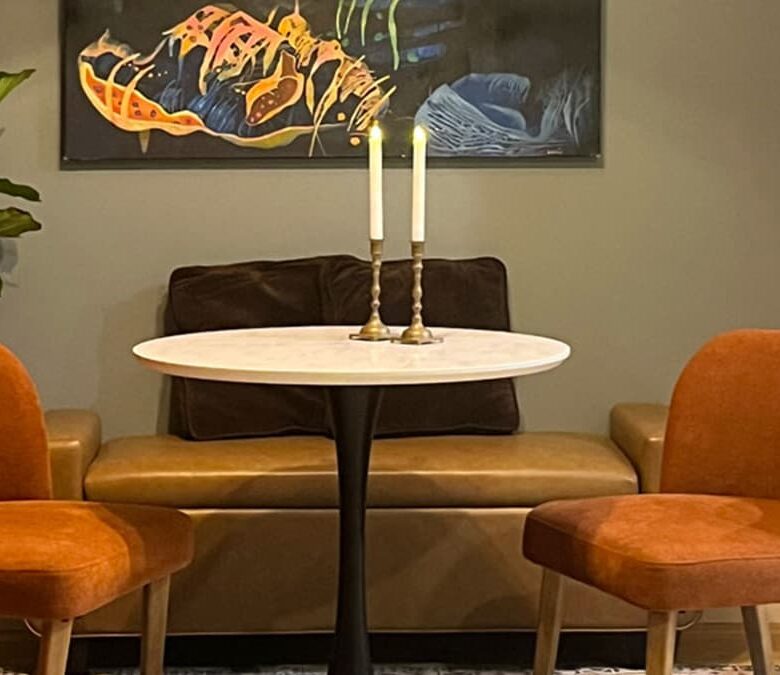 Modern dining nook interior design with orange accent chairs, banquette seating, and round marble table